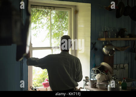Thoughtful senior man looking through window in kitchen at home Stock Photo