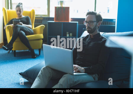 Male executive sitting on arm chair and using laptop in office Stock Photo