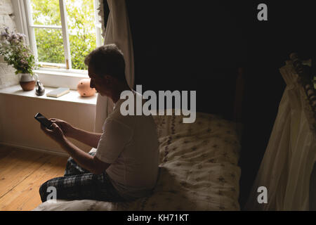 Senior man using mobile phone in bedroom at home Stock Photo
