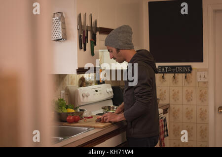 Man cutting vegetables into slices on chopping board in kitchen Stock Photo