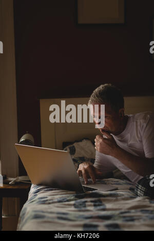 Senior man using laptop in bedroom at home Stock Photo