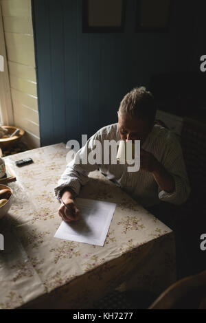 Senior man writing on document paper while having coffee in kitchen at home Stock Photo