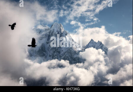 Two flying birds against majestical Manaslu mountain with snowy peak in clouds in sunny bright day in Nepal. Landscape with beautiful high rocks and b Stock Photo