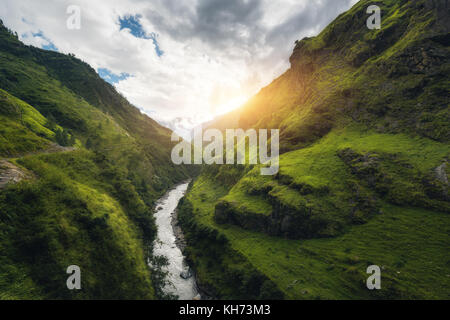 View with amazing Himalayan mountains covered green grass, river, meadows and forest, blue sky with clouds, sun and stones in water in autumn in Nepal Stock Photo