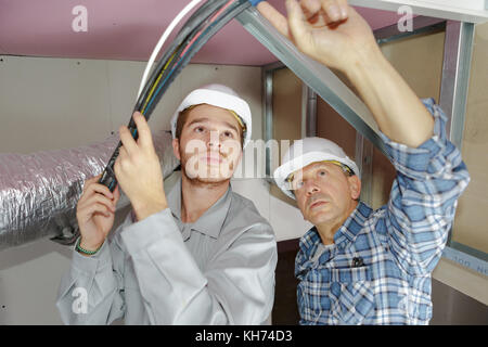 father and son electricians working on buildings ceiling Stock Photo