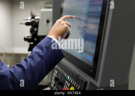 A service engineer using the touch screen to prepare cnc metalworking center for a new task. Selective focus. Stock Photo