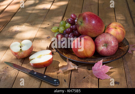 Plate of apples, peaches and grapes with a sliced apple on a wooden surface Stock Photo