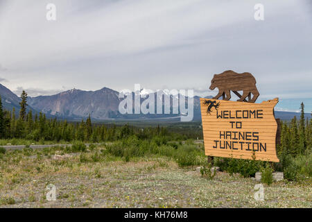 With majestic mountains of Kluane National Park in the background, a wooden sign with bear silhouette welcomes visitors to Yukon town of  Haines Jct Stock Photo