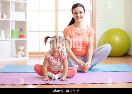 Mother and child daughter practicing yoga together in living room at home. Sport and family concept. Stock Photo