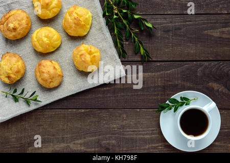 Freshly baked buns eclairs and a cup of coffee (espresso) on a dark wooden background. Light breakfast. The top view. Stock Photo