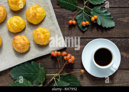 Freshly baked buns eclairs and a cup of coffee (espresso) on a dark wooden background. Light breakfast. The top view. Stock Photo