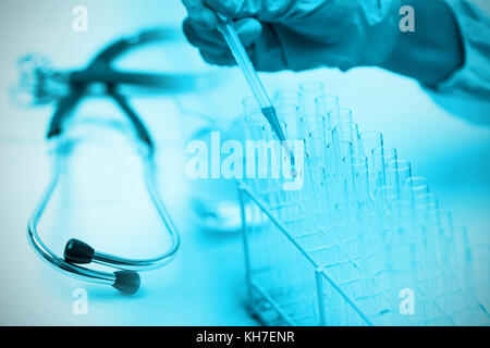 Stethoscope on desk against protected hand dropping dangerous liquid in test tubes Stock Photo
