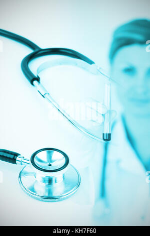 Metal black stethoscope against female scientist looking at the camera while holding a test tube Stock Photo
