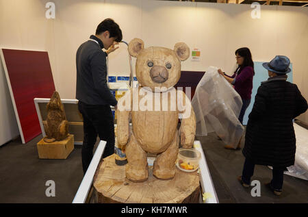 Hamburg, Germany. 14th Nov, 2017. The wooden sculpture 'my old Teddy' by Albrecht Klink can be seen while employees of the Gallery White Birch from Seoul, South Korea set up their stand at the fair 'Affordable Art Fair' in Hamburg, Germany, 14 November 2017. 80 national and international galleries offer works of contemporary artists from 100 up to 7500 euros at the arts fair. The 'Affordable Arts Fair' runs from 16 - 19 November 2017 on the Hamburg Fair grounds. Credit: Georg Wendt/dpa/Alamy Live News Stock Photo