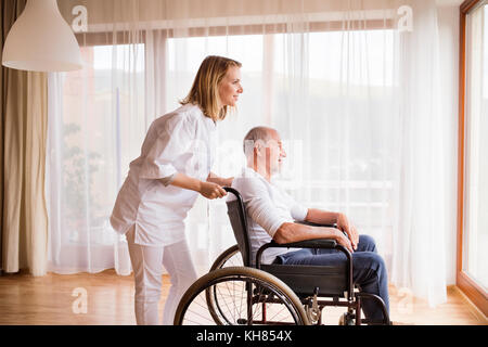 Nurse and senior man in wheelchair during home visit. Stock Photo