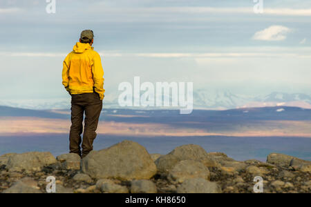 Man standing on mountain, looking relaxed towards snowy mountain range. Stock Photo