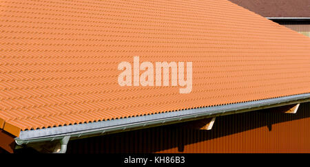 Red tiles roof with rain pipe and corrugated metal wall. Stock Photo