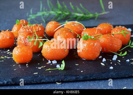 Honey glazed baby carrots with sea salt and thyme on a grey abstract background. Healthy eating concept. Fasting food. Healthy meal Stock Photo