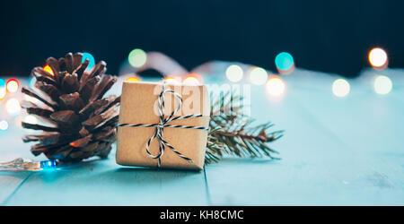 Christmas present with pine cone and fir branch on blue wooden planks and lights bookeh at the background. Shallow depth of field Stock Photo