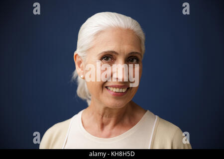 Photo of charming smiling old woman, looking at camera, over dark blue background Stock Photo