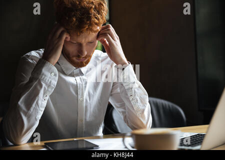 Photo of tired readhead businessman, touching his head, looking at digital tablet Stock Photo