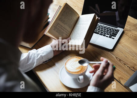 Top view of man in white shirt stirring coffee while reading book Stock Photo