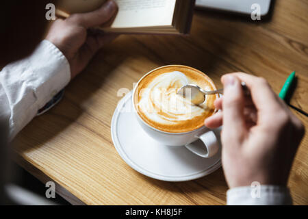 Cropped photo of man in white shirt stirring coffee while reading book Stock Photo