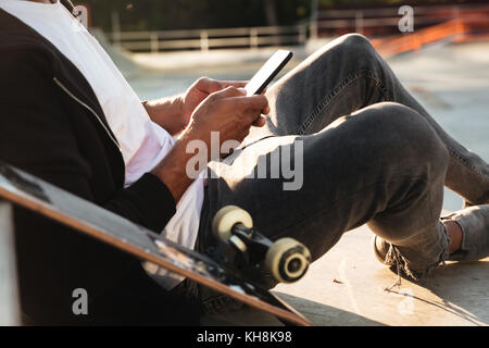 Cropped image of an african man with a skateboard using smartphone while resting in a skating zone Stock Photo