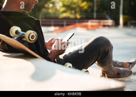 Cropped image of an african guy using mobile phone while having rest in urban zone Stock Photo