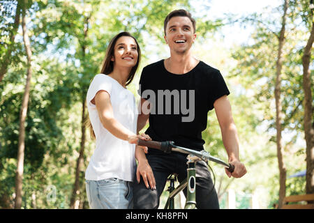 Portrait of a young smiling couple riding on a bicycle together at a park Stock Photo