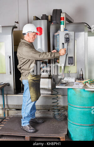 Worker using CNC machine in metallurgy factory Stock Photo