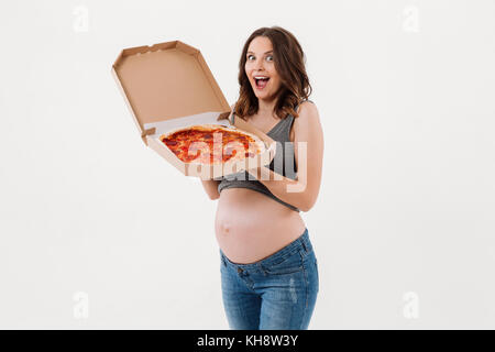 Photo of surprised pregnant woman standing isolated over white background. Looking camera holding pizza. Stock Photo