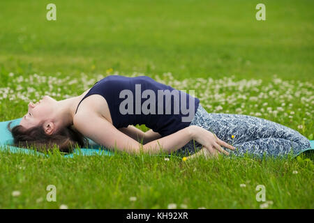 Thin girl doing yoga outside at summer on green grass. Stock Photo