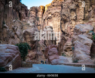 Tourist visitors walking through empty Siq pink sandstone gorge in early morning light, Petra, Jordan, Middle East