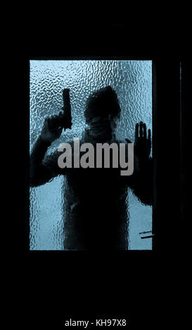 Man holding gun looking through glass pane of house door. Concept image for gun violence, armed robbery, gun crime, organized crime.... Stock Photo