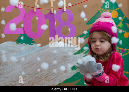 New Year 2018 concept. Beautiful small girl decorating the New Year numeral. background of a painted Christmas tree and snow Stock Photo
