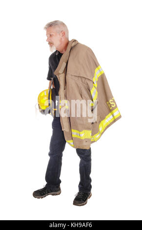 A middle age firefighter man standing in profile with his jacket over his shoulder and helmet in his hand, isolated for white background Stock Photo