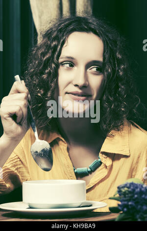 Happy young woman eating a soup at restaurant