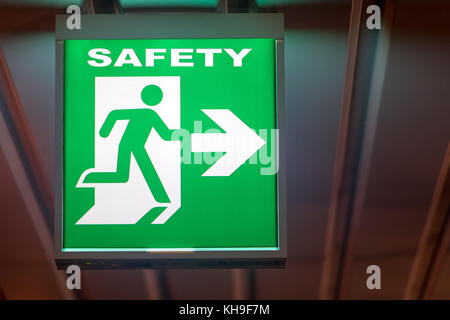 The emergency exit sign shows the direction of safety. The emergency exit board hangs on the ceiling of the building. Stock Photo