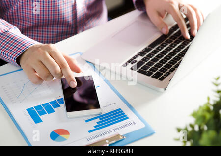 Man using mobile phone while working on laptop. Working with financial statement document Stock Photo