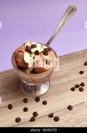 Chocolate Ice Cream in a Glass Cup Topped With Chocolate Chips and Almond Slivers on Purple and Wood Stock Photo