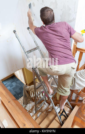 Dangerous tricky position decorating stripping on home stairs on a ladder needing risk assessment health and safety accident looming if careless Stock Photo