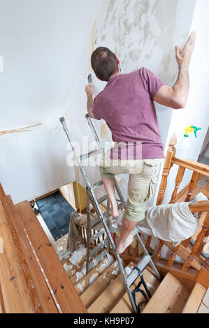 Dangerous tricky position decorating stripping on home stairs on a ladder needing risk assessment health and safety accident looming if careless Stock Photo