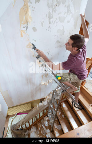 Dangerous tricky position decorating stripping on home stairs on a ladder needing risk assessment health and safety accident looming if careless Stock Photo