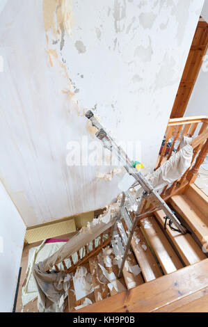 Dangerous tricky position decorating stripping on home stairs on a ladder needing risk assessment health and safety accident looming if careless Stock Photo