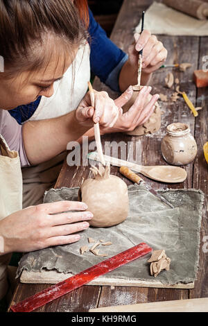 Pottery lesson: a woman potter paints a candlestick from clay, and another woman sculpts a candlestick on a wooden table with tools, brushes in a beau Stock Photo