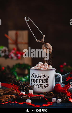 Hot chocolate with marshmallows and flying cocoa powder in Christmas scene with gifts. Action photography with flying strainer