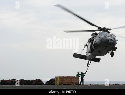 Sailors prepare to attach cargo to an MH-60S Sea Hawk helicopter assigned to the “Eightballers” of He Stock Photo