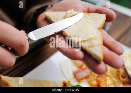 hand with a knife smears butter on bread close-up on a breakfast background Stock Photo