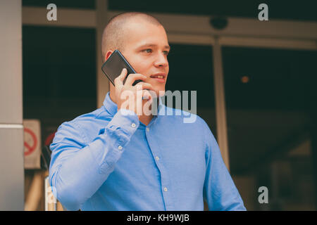 Portrait of cheerful young man looking sideways while talking on smartphone outdoors. Happy handsome man using mobile phone, making call on the street Stock Photo
